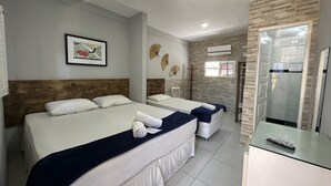 A hotel room with two beds, a wooden headboard, a framed picture, a standing fan, and an air conditioning unit. - Pousada Girassol (Ipojuca)