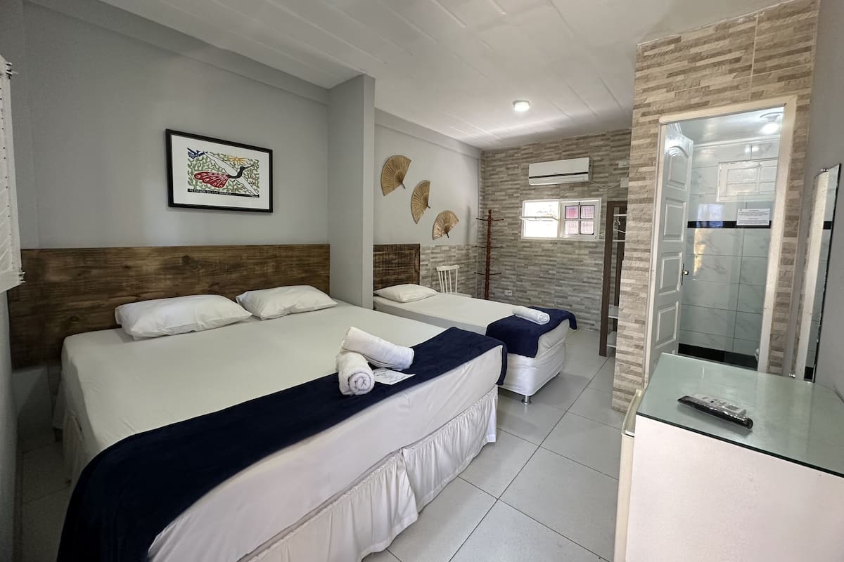 Habitación de hotel con dos camas, cabecero de madera, un cuadro enmarco, ventilador de pie y aire acondicionado.