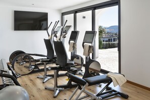 Uma academia com equipamentos de exercícios, uma TV na parede e vista para o exterior.