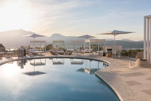 A pool area with lounge chairs and umbrellas, surrounded by a glass enclosure, with mountains in the background. - Sulia House Porto Rotondo, Curio Collection by Hilton (Olbia)