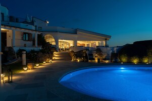 Una villa moderna con piscina, iluminación exterior y un jardín bien cuidado.
