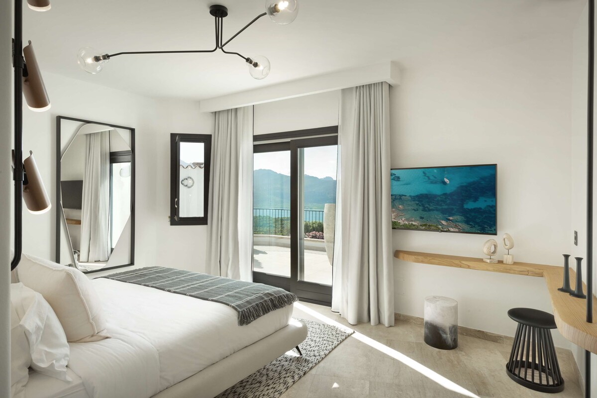 A modern bedroom with a bed, a large window, a painting, and a small stool.