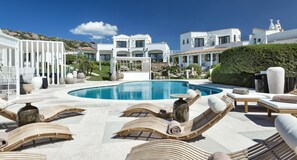 A pool area with lounge chairs and a white building in the background. - Sulia House Porto Rotondo, Curio Collection by Hilton (Olbia)