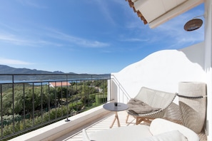 A balcony with a white wall, a wicker chair, a small round table, and a view of the sea and mountains. - Sulia House Porto Rotondo, Curio Collection by Hilton (Olbia)