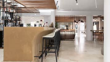 Un espace bar moderne avec un comptoir incurvé et de nombreux tabourets. Un escalier mène à un niveau supérieur, et on aperçoit à l’arrière-plan un coin salon avec des tables et des chaises.
