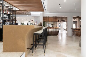 A modern bar area with a curved counter and multiple stools. There is a staircase leading to an upper level, and a seating area with tables and chairs in the background. - Sulia House Porto Rotondo, Curio Collection by Hilton (Olbia)