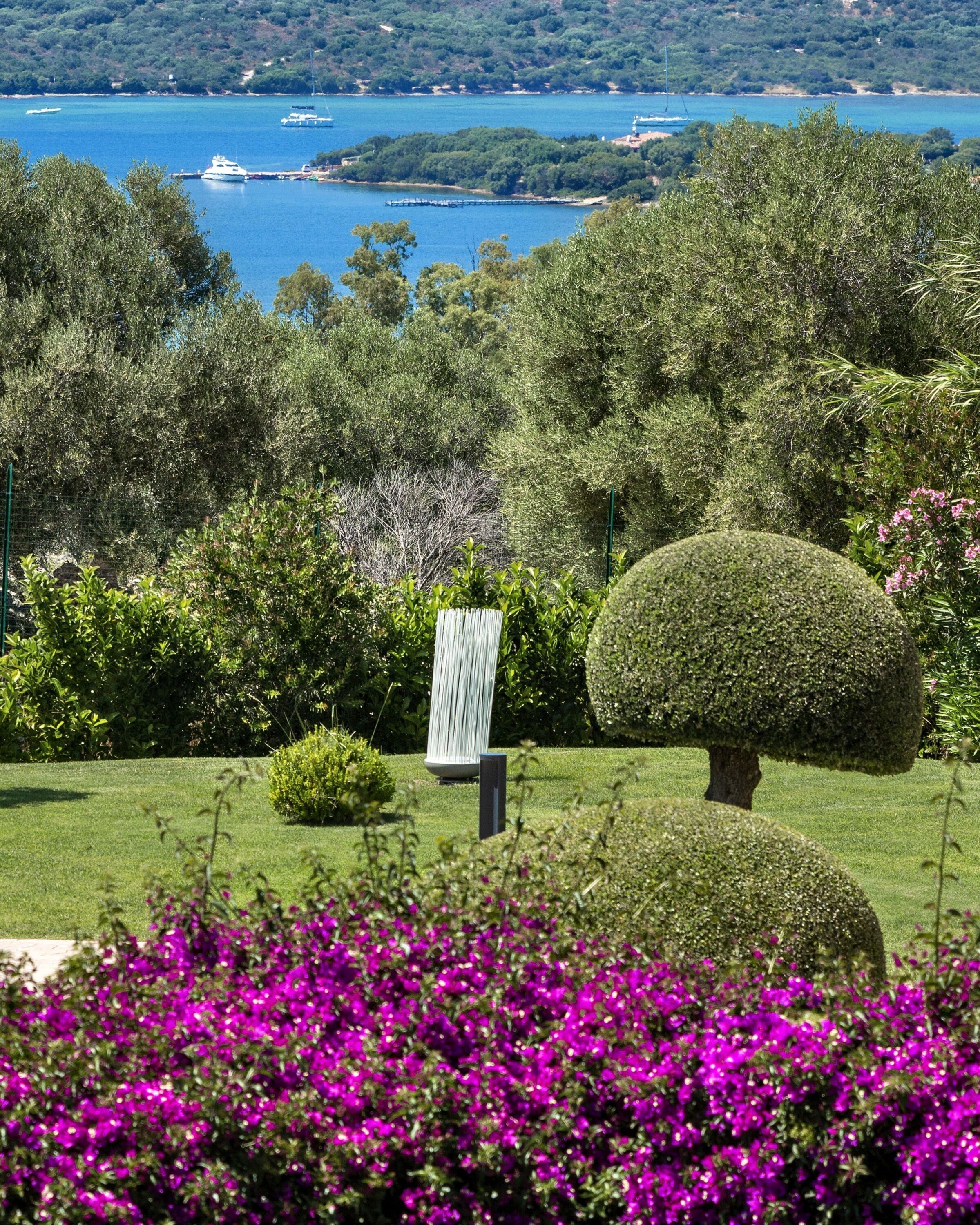 A landscaped garden with neatly trimmed bushes, a spherical topiary, and vibrant purple flowers in the foreground.