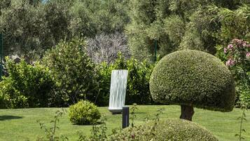 Un jardin aménagé avec des arbustes taillés avec soin, un topiaire sphérique et, au premier plan, des fleurs violettes aux couleurs vives.