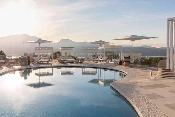 A pool area with lounge chairs and umbrellas, surrounded by mountains. - Sulia House Porto Rotondo, Curio Collection by Hilton (Olbia)