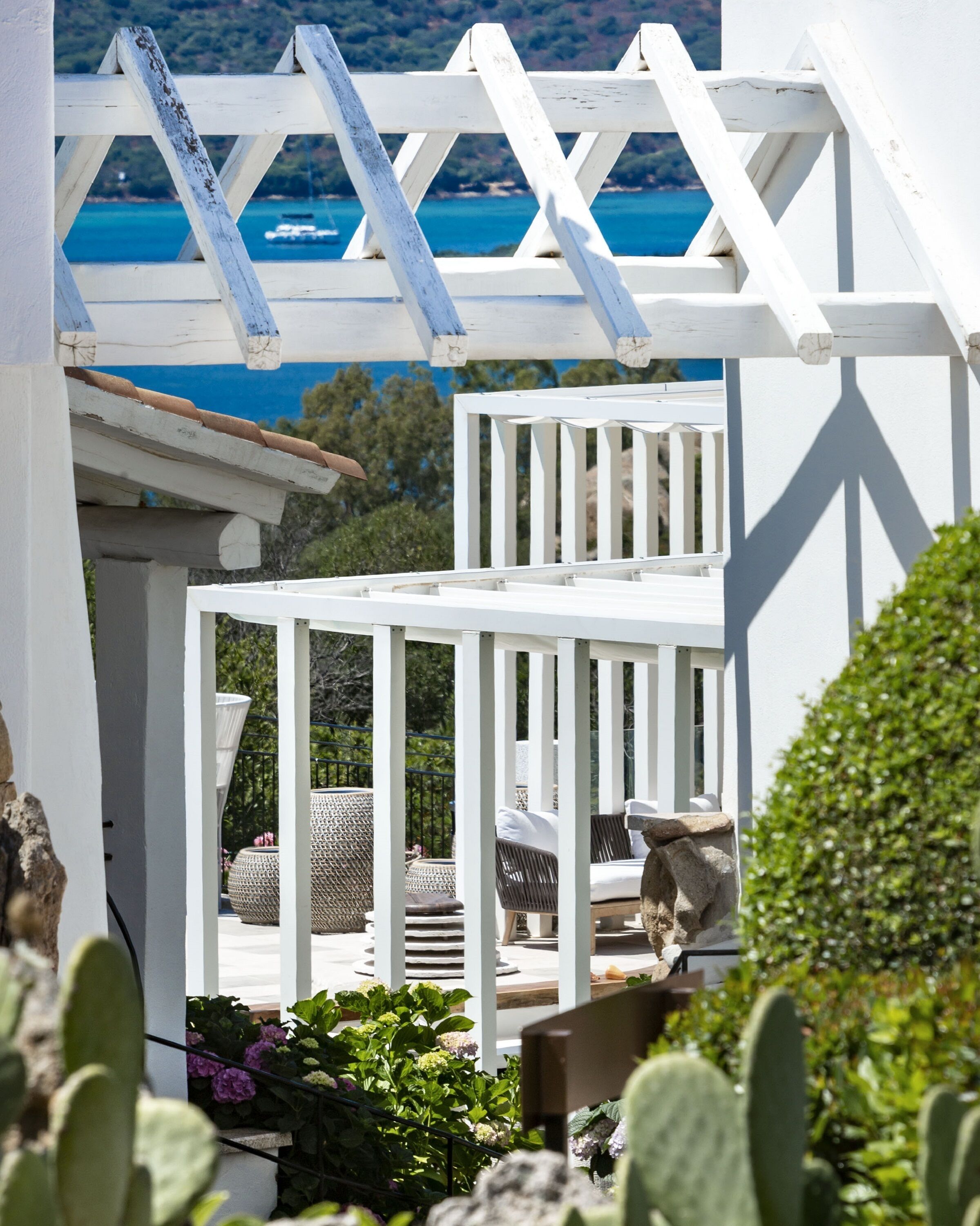 A white pergola structure with a view of the sea and greenery in the background.