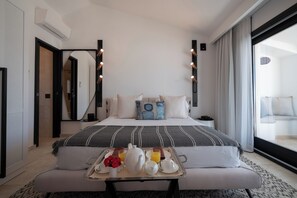 Quarto de hotel moderno com uma cama grande, uma mesinha de cabeceira com uma bandeja de itens de café da manhã e uma janela ampla com cortinas.
