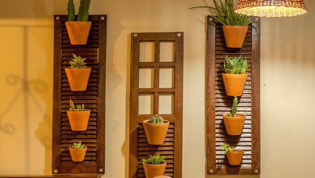 Una pared con listones de madera verticales que sostienen macetas de terracota con plantas.
