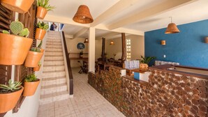 Vestíbulo de hotel con una escalera, una recepción y varias plantas en macetas.
