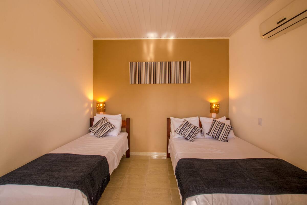 Une chambre double avec deux lits, chacun équipé d’un oreiller et d’une couverture, d’un climatiseur mural et d’une décoration murale à rayures.