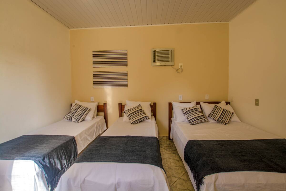 Une chambre d’hôtel avec deux lits simples, chacun équipé d’un oreiller et d’une couverture. On y trouve deux climatiseurs fixés au mur et un interrupteur pour la lumière, également fixé au mur.