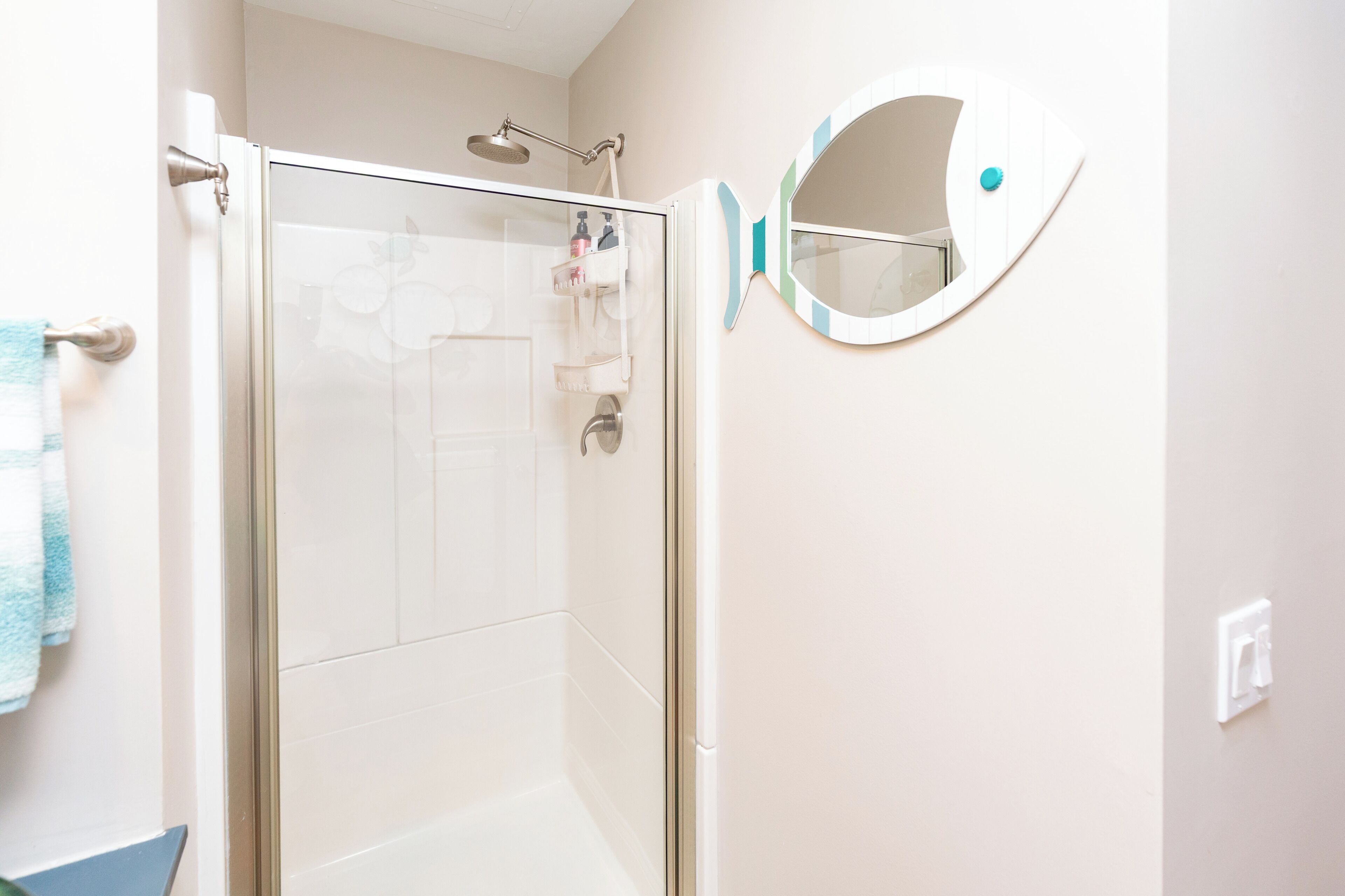 A bathroom with a glass shower door, a round mirror, and a towel rack.