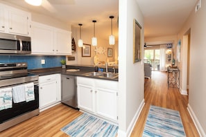 A modern kitchen with white cabinets, stainless steel appliances, and a blue backsplash. - Ocean Glass Inn Condominiums (Rehoboth Beach)
