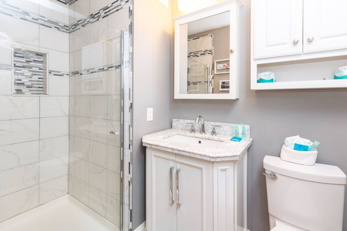 A bathroom with a glass shower enclosure, a marble sink, and white cabinetry.