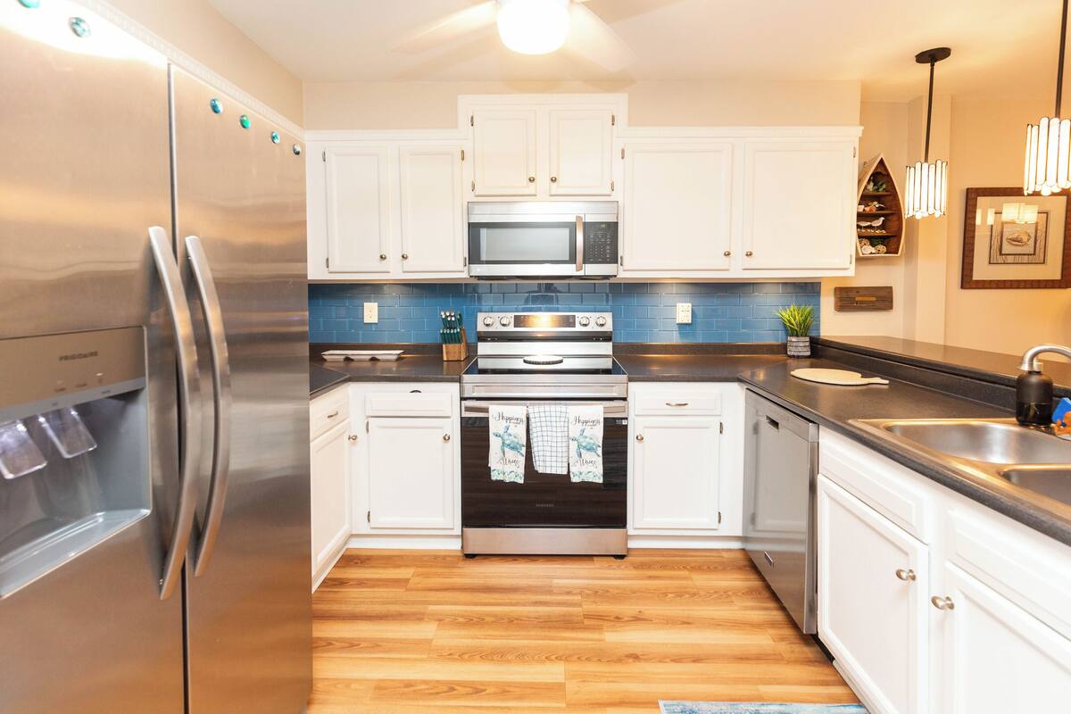 A modern kitchen with stainless steel appliances, white cabinetry, and a blue backsplash.