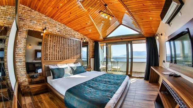A bedroom with a large bed, wooden ceiling, and a view of the sea. - Diamond Liman Hotel (Amasra)