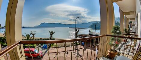 A balcony with a view of a body of water, mountains, and a clear sky.
