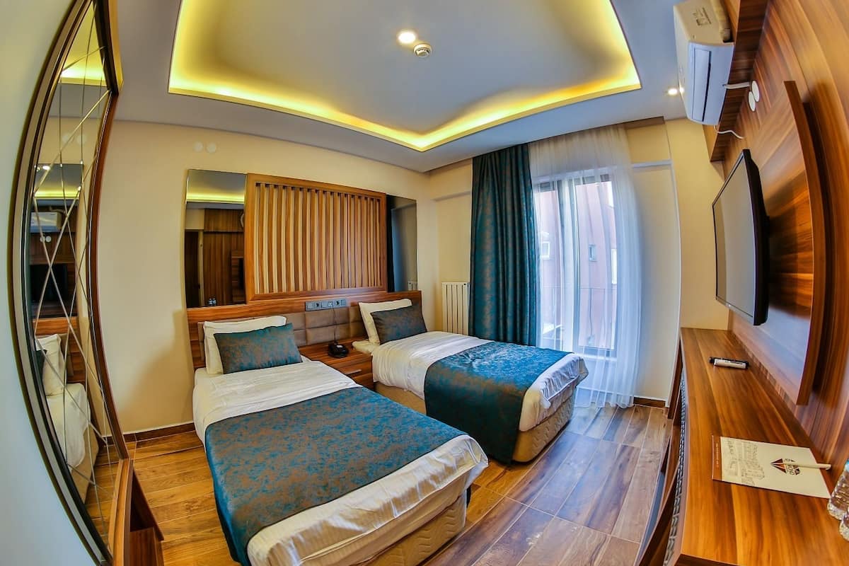 A modern hotel room with two beds, a large mirror, a TV, and a wooden floor.