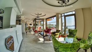 A spacious hotel lobby with a reception desk, comfortable seating, and large windows offering a view of the sea. - Diamond Liman Hotel (Amasra)