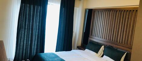 A hotel room with a large bed, a wooden headboard, and a view of the outside through the window.