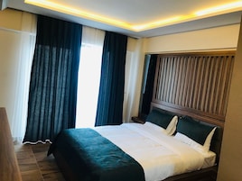 Quarto de hotel com uma cama grande, cabeceira de madeira e vista para o exterior pela janela.
