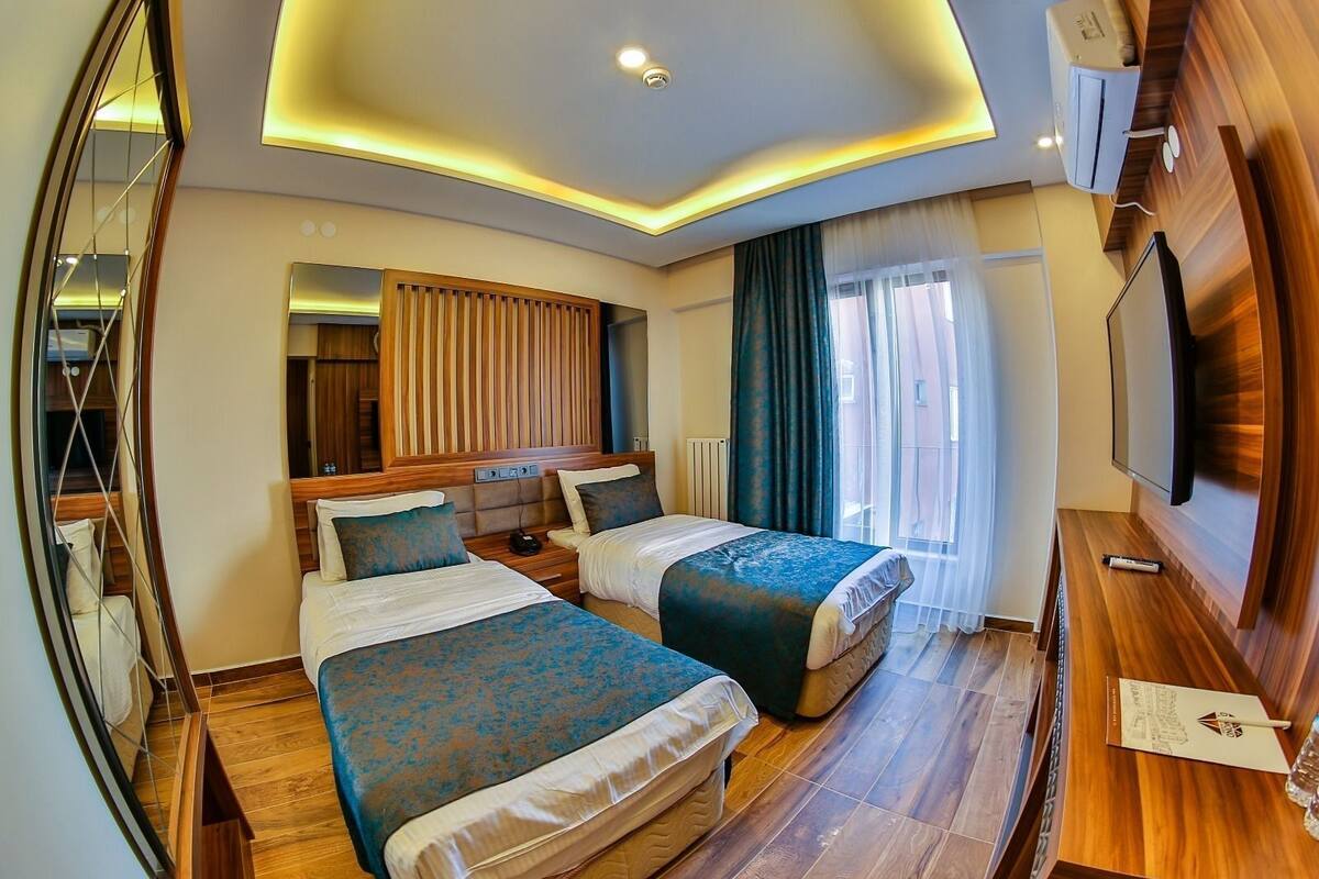 A hotel room with two beds, a TV, a mirror, and a wooden floor.