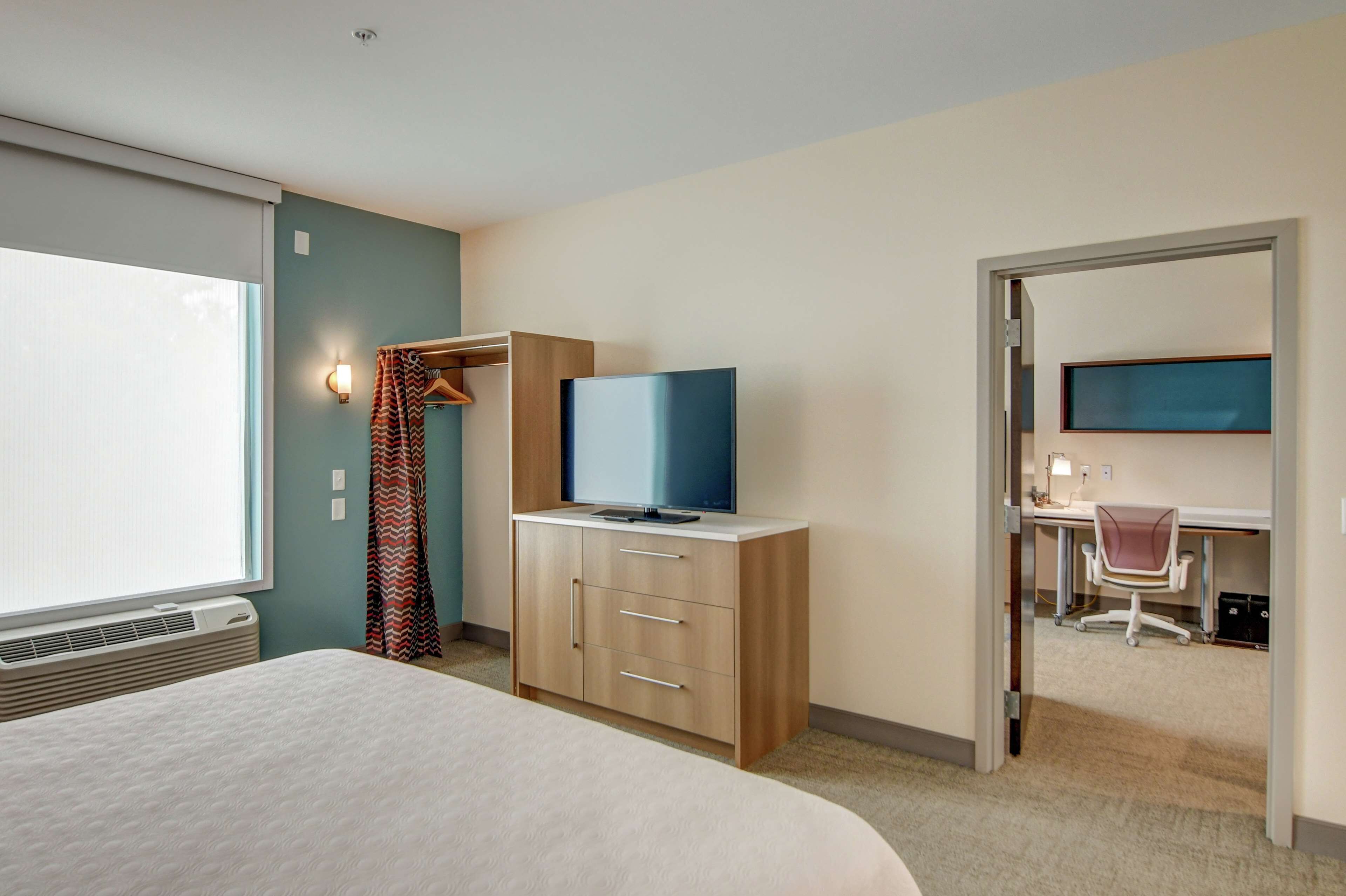 A hotel room with a bed, a TV on a wooden cabinet, a desk with a chair, and a wardrobe with a mirror.