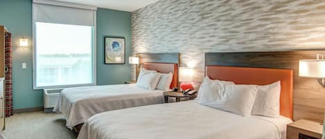 A hotel room with two beds, a large window, a wall-mounted heater, and a view of the outdoors.