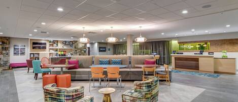 A modern hotel lobby with a seating area, a reception desk, and a television screen.