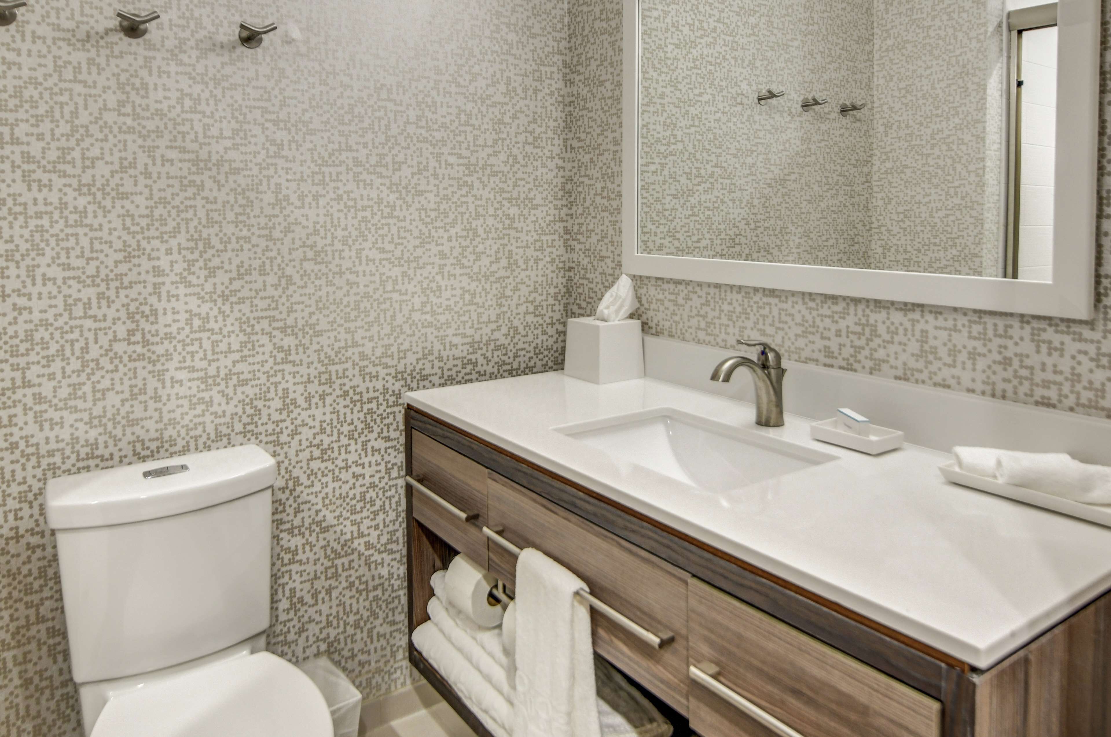 Une salle de bain moderne avec des toilettes blanches, un lavabo surmonté d’un miroir et un porte-serviettes.