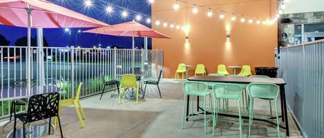 An outdoor patio with tables and chairs, string lights, and umbrellas.