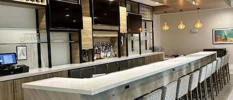 A modern bar area with a long counter, bar stools, and a wine rack.