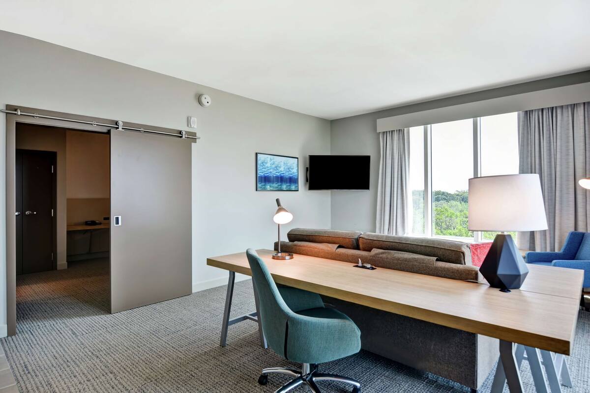A hotel room with a desk, a sofa, a TV, and a window with curtains.