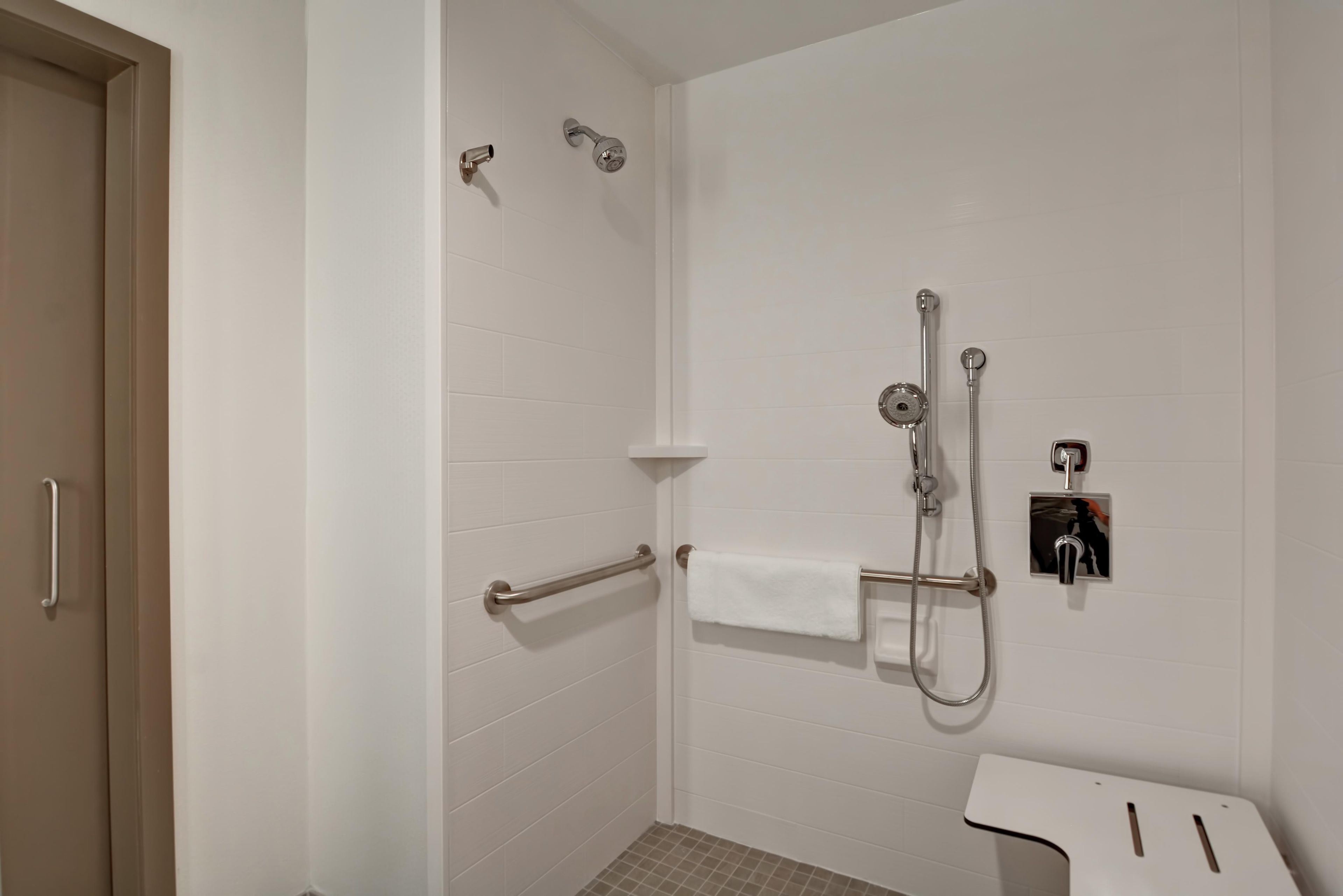 Une salle de bain avec des murs recouverts de carreaux blancs, une douche avec un pommeau de douche amovible, un porte-serviettes et des toilettes avec un abattant blanc.