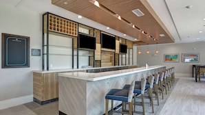 A modern bar area with a long counter, multiple TVs, and a row of bar stools. - Hilton Garden Inn Biloxi (Biloxi)