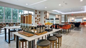 A modern dining area with high tables, bar stools, and a variety of food containers. - Hilton Garden Inn Biloxi (Biloxi)