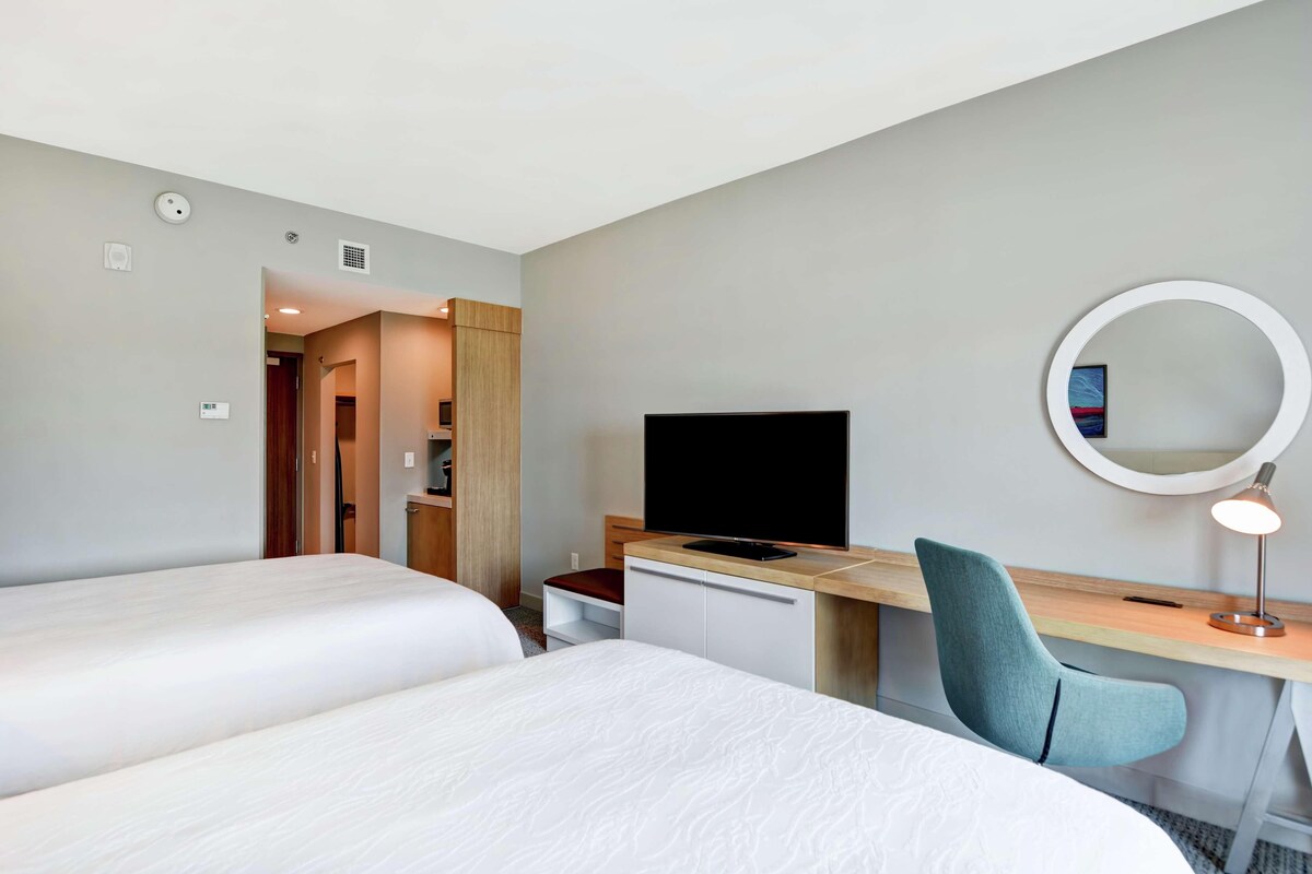 Habitación de hotel con dos camas, un escritorio, un televisor, un espejo y una lámpara de escritorio.