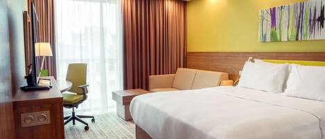Habitación de hotel con una cama grande, un escritorio con lámpara, una silla y un cuadro en la pared.