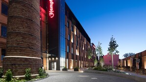 A modern building with a prominent red sign, large windows, and a brick facade. - Hampton by Hilton Kalisz (Kalisz)
