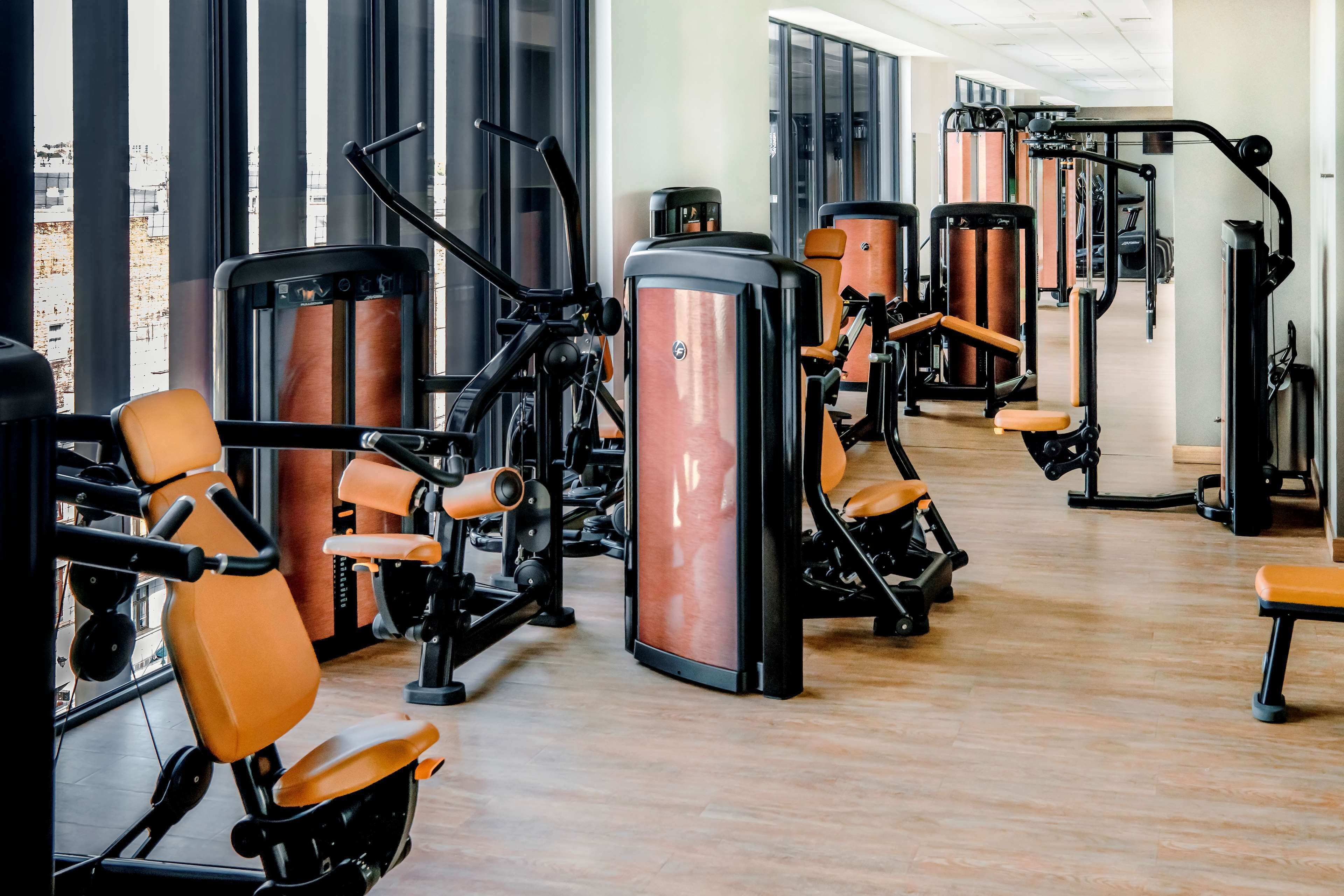Et fitnesscenter med diverse træningsmaskiner, store vinduer og trægulv.