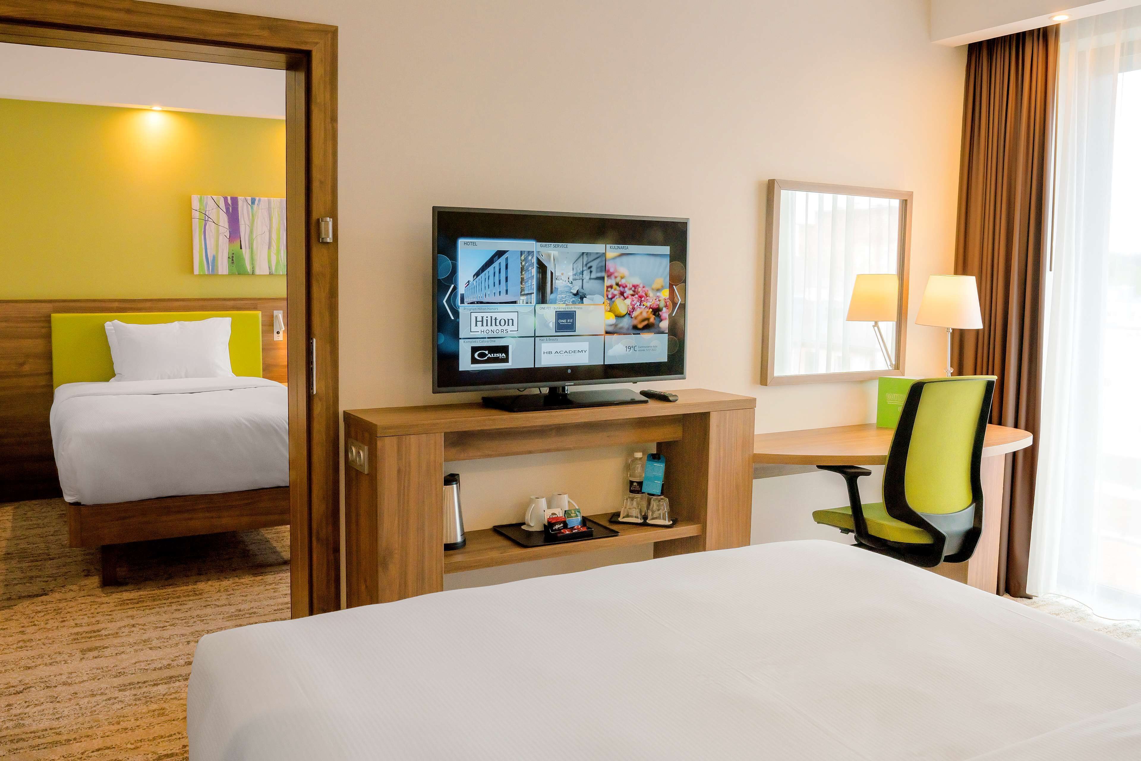 Une chambre d’hôtel avec un lit, un téléviseur posé sur un meuble en bois, un bureau avec une chaise et une fenêtre avec des rideaux.