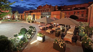 An outdoor dining area with tables and chairs, surrounded by flower beds and a building with a sign reading "MARYSIENKA". - Hampton by Hilton Kalisz (Kalisz)
