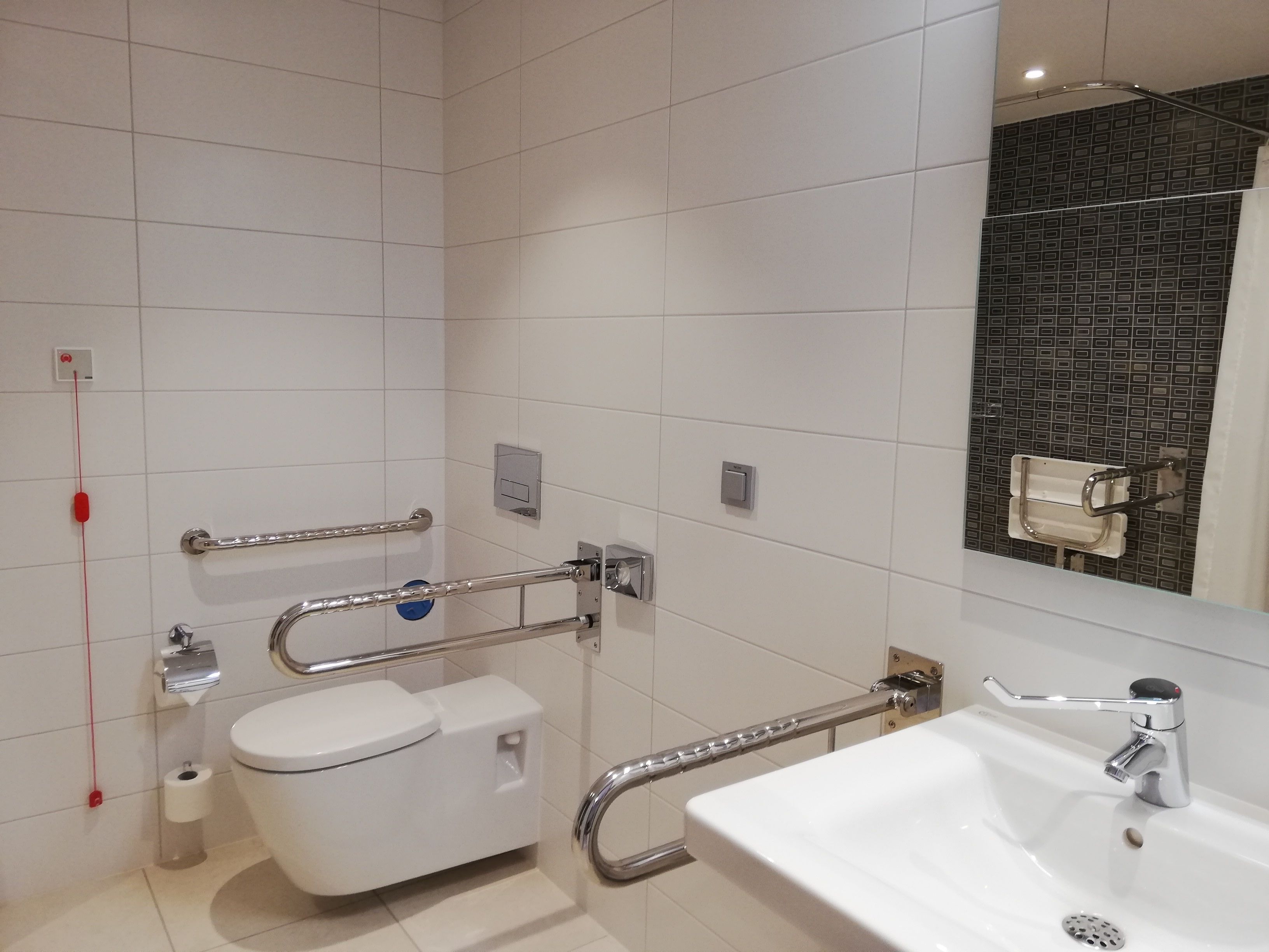 Un baño moderno con inodoro blanco, lavamanos y espejo.