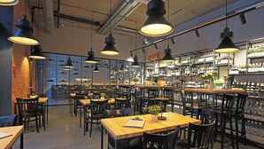 A restaurant with multiple tables and chairs, a bar area with shelves of bottles, and hanging pendant lights. - Hampton by Hilton Kalisz (Kalisz)