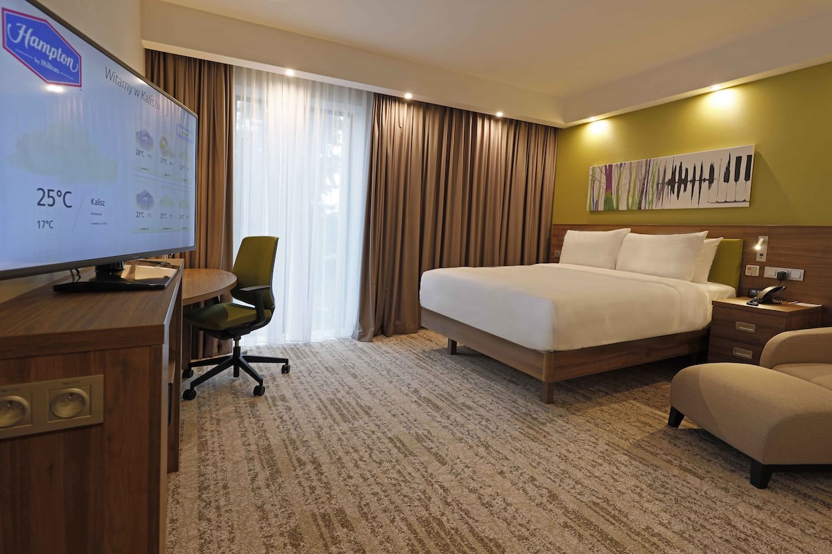 Quarto de hotel com cama, escrivaninha com computador, cadeira e televisão mostrando a temperatura do quarto.
