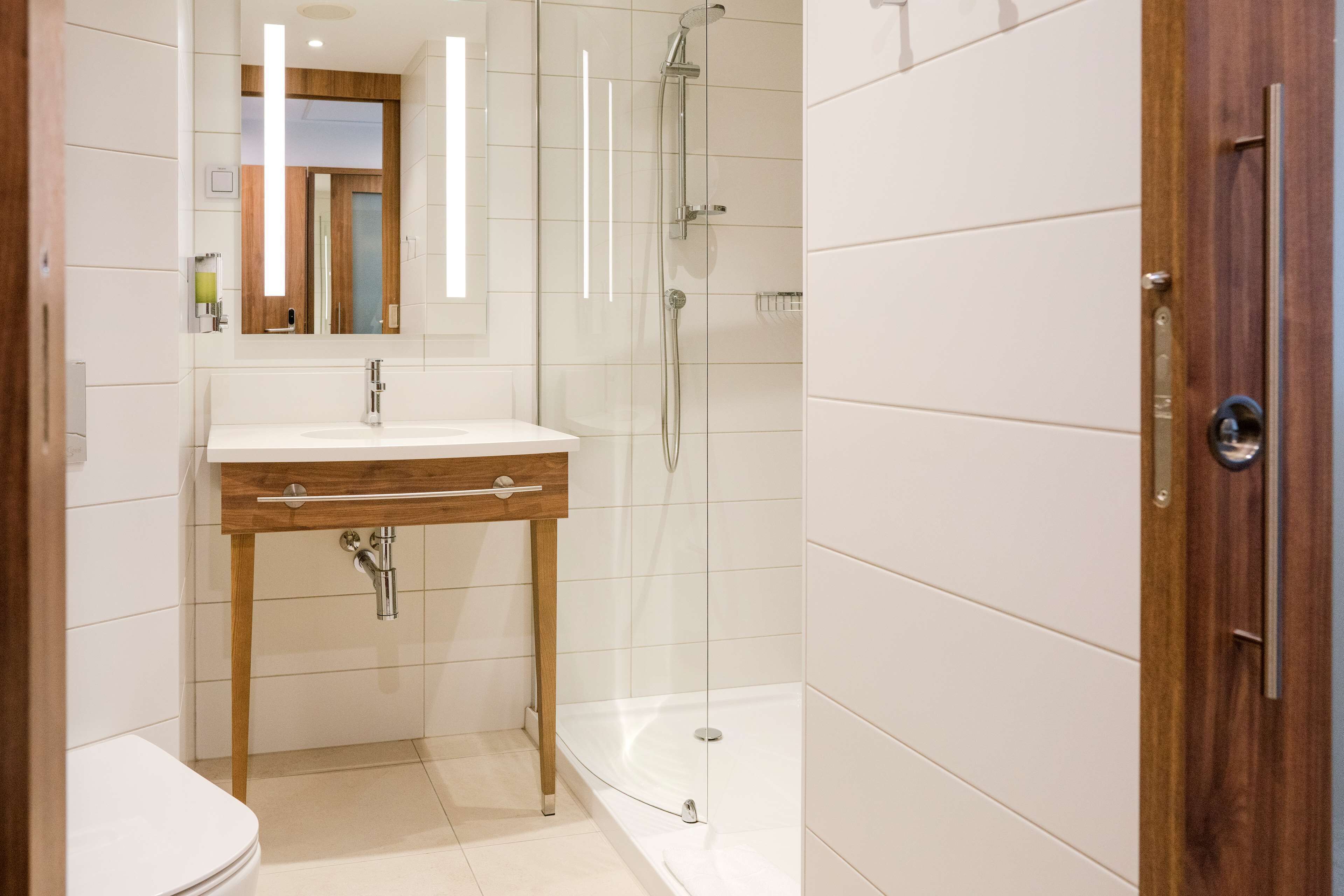 A modern bathroom with a wooden vanity, a glass shower enclosure, and a white tiled floor.